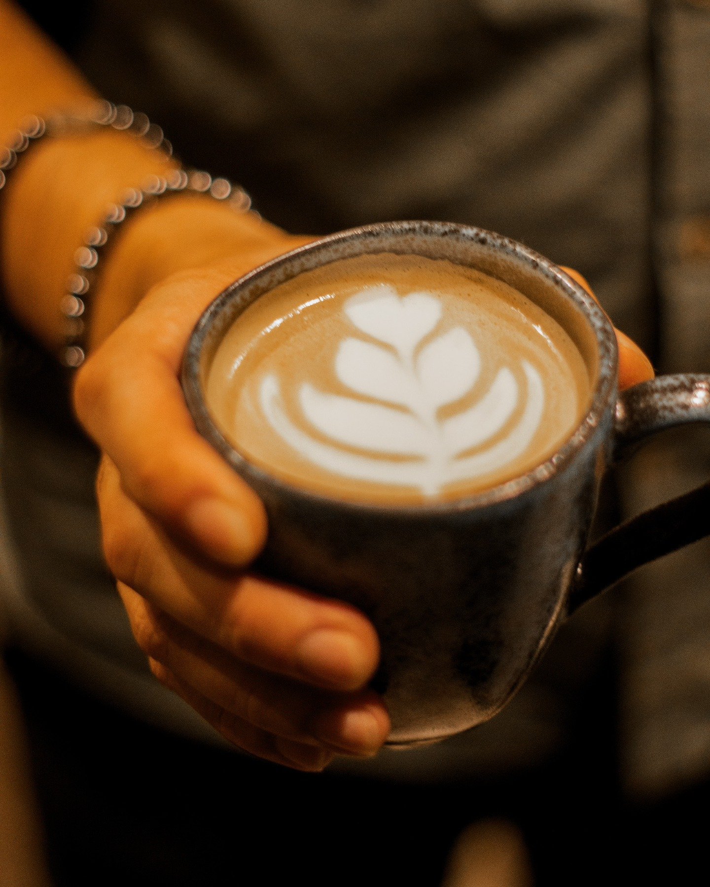 Mão segurando uma caneca de cerâmica com latte e desenho de tulipa